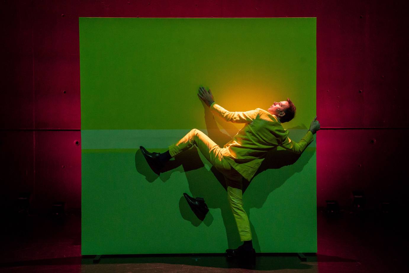 A man in a yellow suit tries to climb a green-lit wall